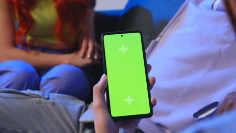 Close-Up-Of-Woman-With-Green-Screen-Mobile-Phone-Sitting-On-Sofa-At-Home-With-Friends-1